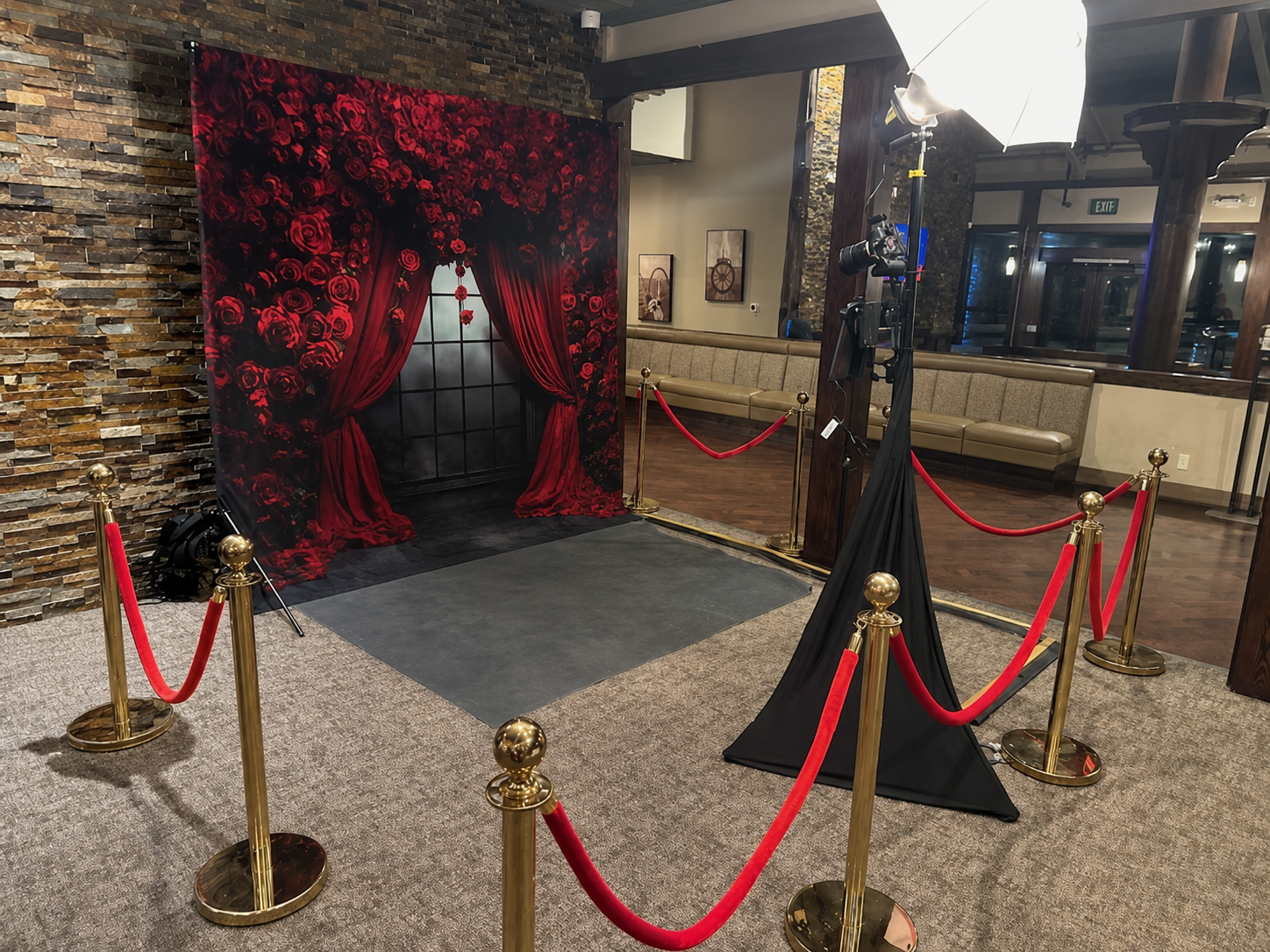 Valentine’s Day photography setup with a red rose backdrop, professional camera lighting, and brass stanchions with red velvet ropes.